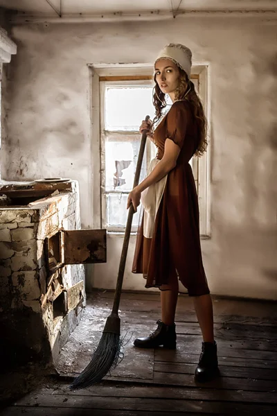Mujer en un vestido rústico barre el suelo de madera en la cocina — Foto de Stock