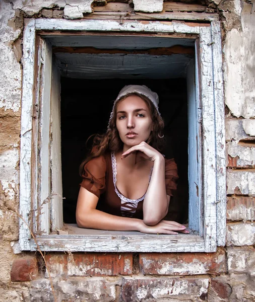 Donna triste in un vestito rustico seduto vicino alla finestra nella vecchia casa si sentono soli. Stile Cenerentola — Foto Stock