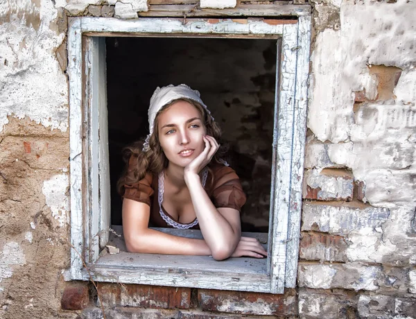 淋しい古い家の窓の近くに座っている素朴なドレスの悲しい女。シンデレラ スタイル — ストック写真