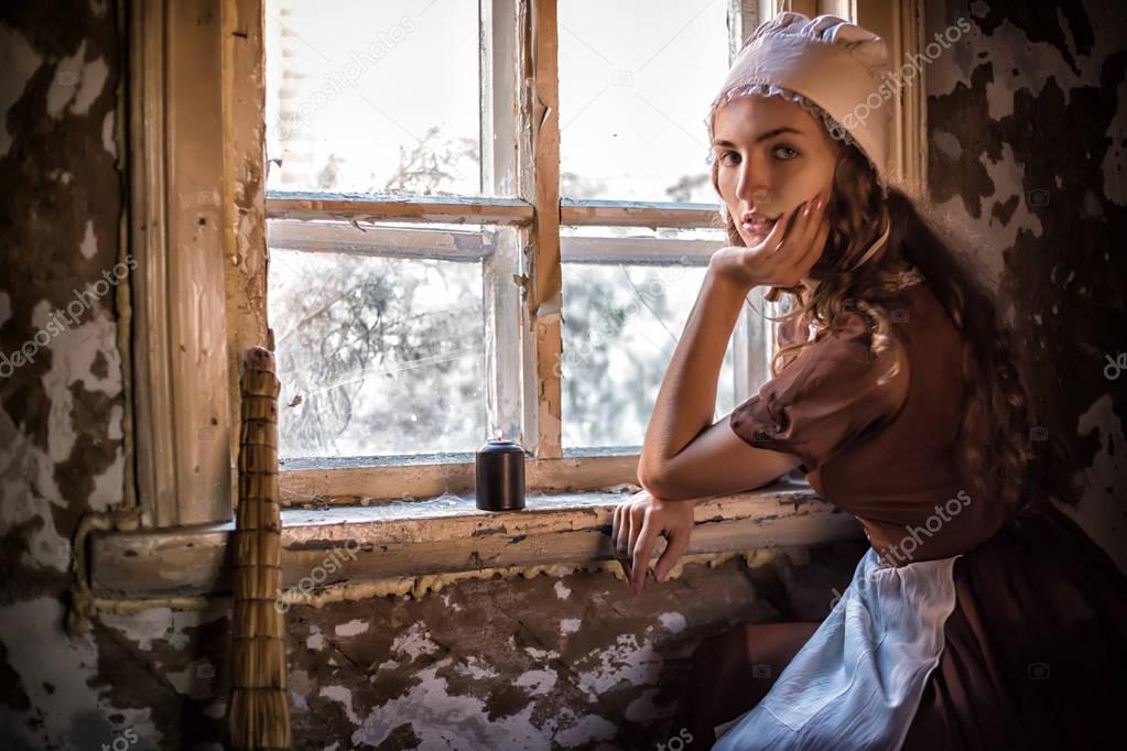 sad woman in a rustic dress sitting near window in old house feel lonely. Cinderella style