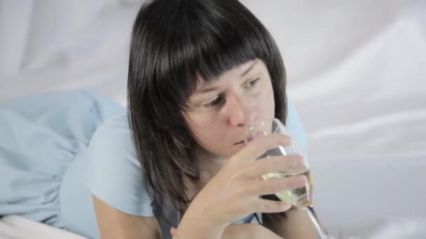 Jovem mulher atraente solitário encontra-se em uma cama em um quarto, bebe champanhe — Vídeo de Stock