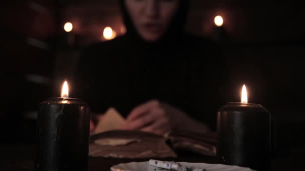 Freira bonita mística em um vestido preto, freira lê um livro velho com luz de velas preta — Vídeo de Stock