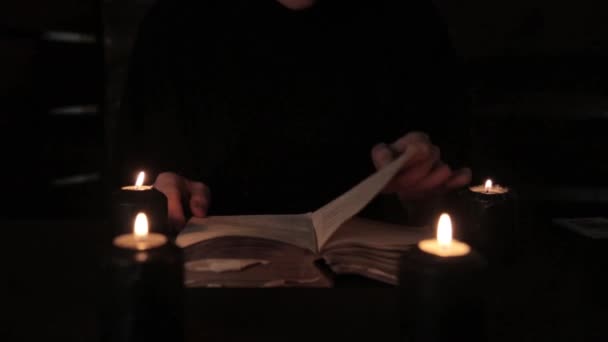 Μυστικιστική όμορφη μάγισσα σε ένα μαύρο φόρεμα, ρίχνει ένα ξόρκι από το παλιό βιβλίο με μαύρο φως των κεριών — Αρχείο Βίντεο