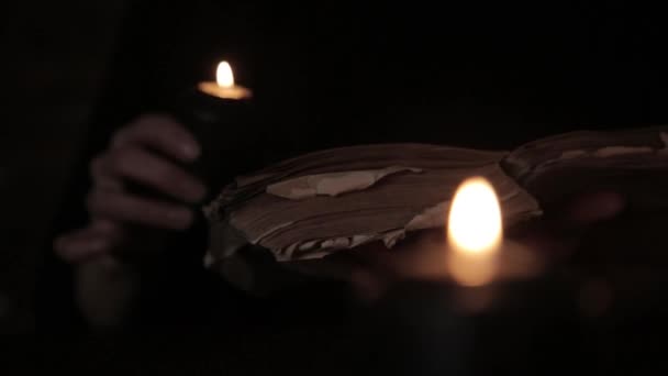 Μυστικιστική όμορφη μάγισσα σε ένα μαύρο φόρεμα, ρίχνει ένα ξόρκι από το παλιό βιβλίο με μαύρο φως των κεριών — Αρχείο Βίντεο