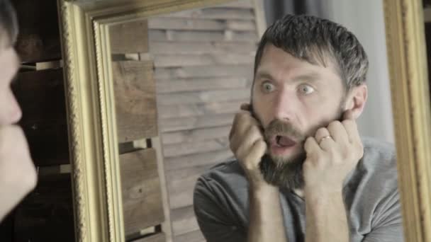 Вульгарний чоловік жорстоко подряпає бороду перед дзеркалом — стокове відео