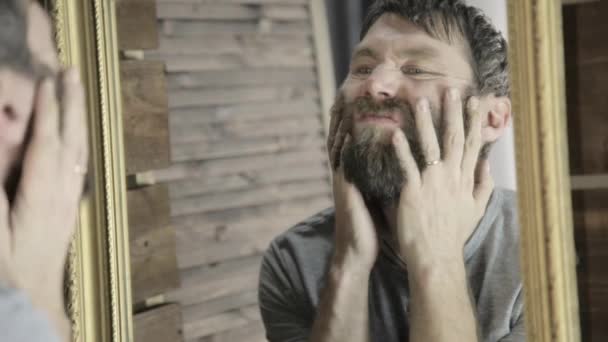 Vulgar hombre brutalmente se rasca la barba delante del espejo — Vídeos de Stock