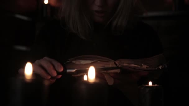 Відьма тримає ніж і читає заклинання зі старої чарівної книги, запаленої чорними свічками — стокове відео