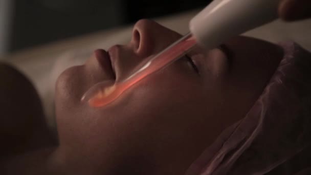 Косметолог делает электрический дарсонвальный массаж для клиентки в темноте — стоковое видео