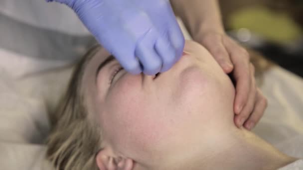 Косметолог-дерматолог делает массаж губ красивой женщине в салоне красоты — стоковое видео