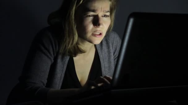 Жінка в окулярах за допомогою комп'ютера в темній кімнаті, дивиться на монітор і починає радіти — стокове відео