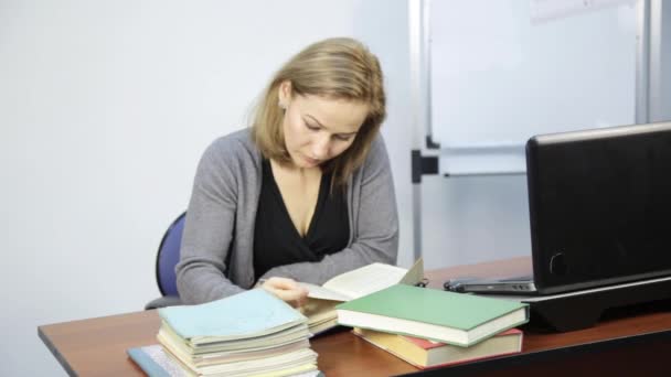 Estudiante lee libro delante de la computadora portátil — Vídeos de Stock