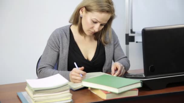 Vrouwelijke student leest en notities maakt in een boek voor laptop — Stockvideo