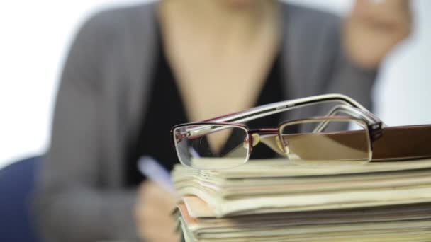 Lunettes sur une pile de cahiers d'exercices et femme d'affaires avec fond flou focus — Video