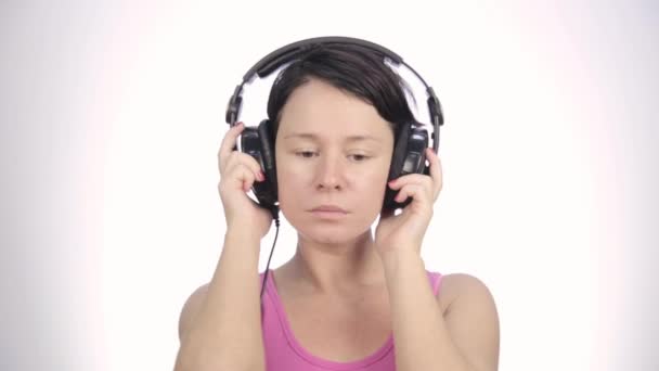 Mooie vrouw dansen in koptelefoon terwijl u luistert naar een muziek op een lichte achtergrond — Stockvideo