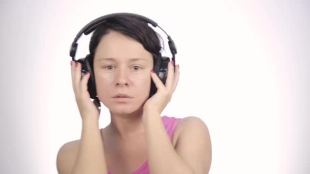 Brunett kvinna lyssna musik med stora hörlurar och dansar på en ljus bakgrund — Stockvideo