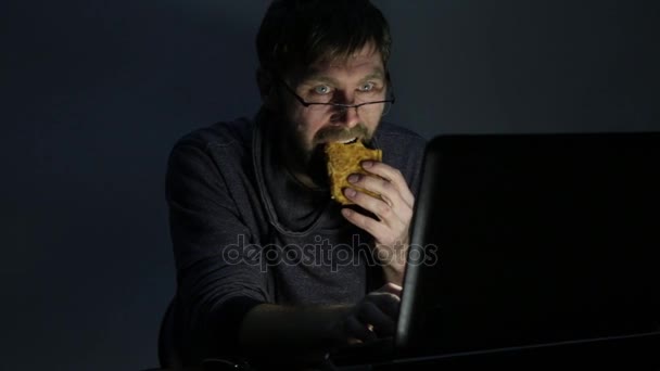 Hombre barbudo comiendo sándwich delante de una computadora portátil — Vídeos de Stock