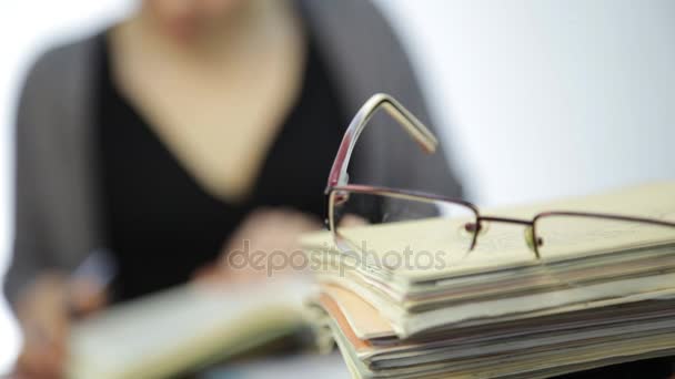 練習帳の山の上の眼鏡、女性は視力矯正後メガネなし動作します。 — ストック動画