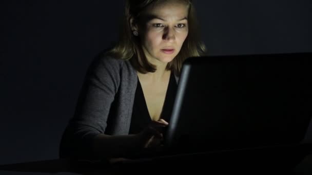 Mujer trabajadora que trabaja en el ordenador portátil y toma notas en el cuaderno en la habitación oscura — Vídeo de stock