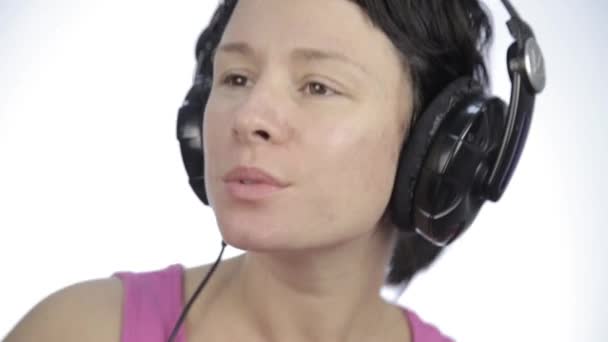 Hermosa mujer bailando en auriculares mientras escucha una música sobre un fondo claro — Vídeos de Stock