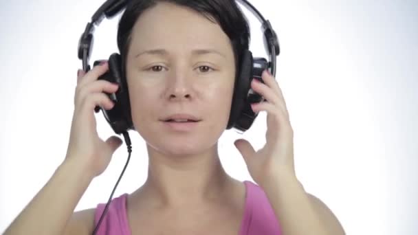 Mujer morena escuchando música con auriculares grandes y bailando sobre un fondo claro — Vídeos de Stock