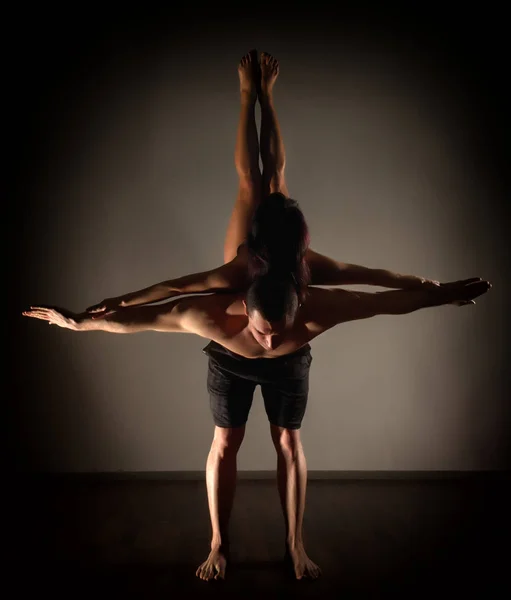 Mladý sportovní pár dělá acroyoga cvičení v temné místnosti — Stock fotografie