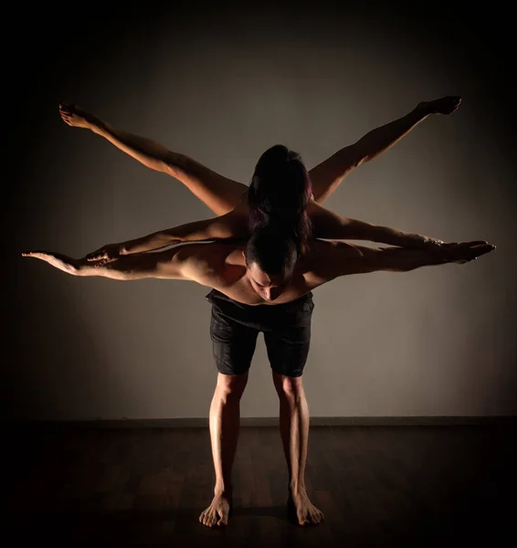 Giovane coppia sportiva che fa esercizi di acroyoga in una stanza buia — Foto Stock