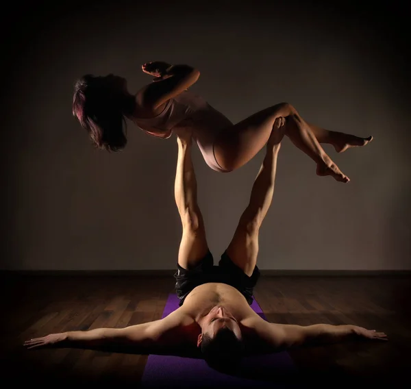 Sports man and woman doing acroyoga exercises in a dark room — Stock Photo, Image
