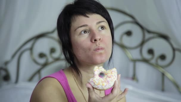 Mujer comiendo un donut en una cama, desayuno con comida chatarra — Vídeo de stock