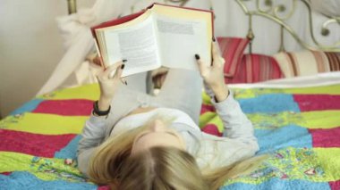 Güzel genç kadın evde bir yatak üzerine bir kitap okuma