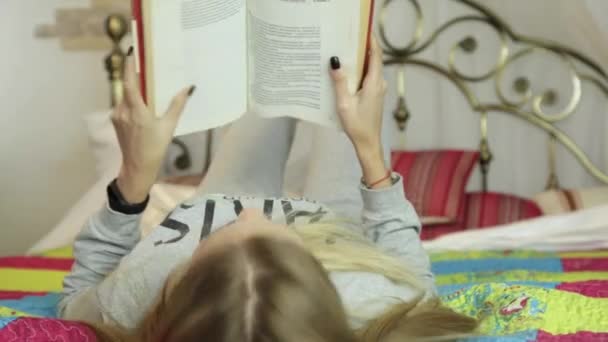 Mujer joven aprendiendo en casa. chica leyendo un libro en una cama — Vídeos de Stock