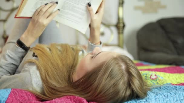 O tânără care învață acasă. Fata citind o carte pe un pat — Videoclip de stoc