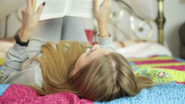 Молодая женщина учится дома. девушка читает книгу на кровати — стоковое видео