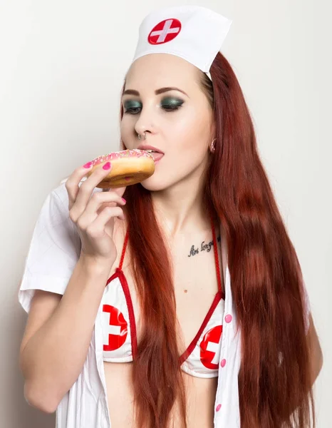 Jovem mulher sexy no terno de enfermeira comer donuts, pessoal médico sexual — Fotografia de Stock