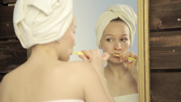 Ung vacker kvinna med handduk på en huvud borsta hennes tänder i badrum — Stockvideo