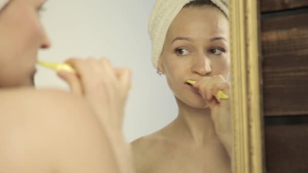 Νεαρή όμορφη γυναίκα με πετσέτα σε ένα κεφάλι βουρτσίζετε τα δόντια της στο μπάνιο — Αρχείο Βίντεο