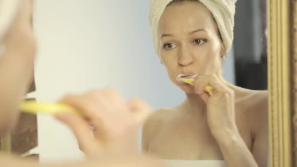 Tükörképét a tükörben gyönyörű nő a fejét a fogmosás a fürdőszobában törölköző — Stock videók