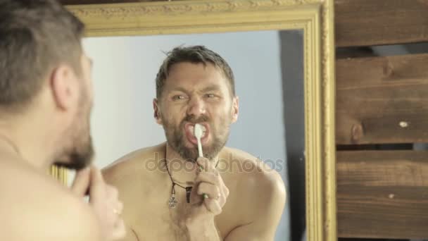 Homem barbudo escovando os dentes na frente do espelho no banheiro — Vídeo de Stock