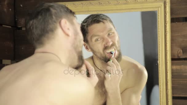 Baard man poetsen zijn tanden in de voorkant van spiegel in badkamer — Stockvideo