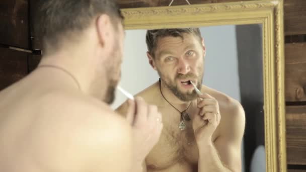 Homem barbudo escovando os dentes na frente do espelho no banheiro — Vídeo de Stock