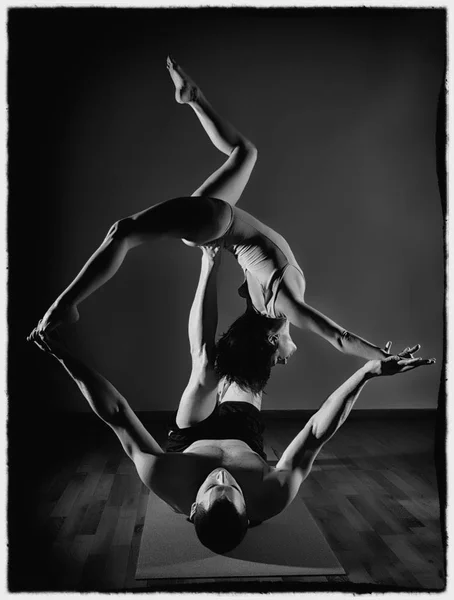 Sports man and woman doing acroyoga exercises in a dark room. black and white — Stock Photo, Image