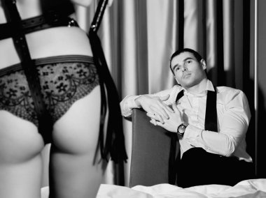 Yakışıklı adam önünde bir kırbaç konumu olan iç çamaşırı baskın seksi kadının kıçından. BDSM kavramı