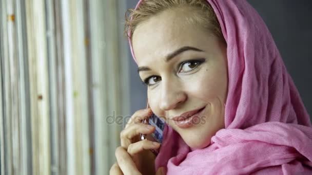 Beautiful muslim woman talking on the phone in front of window — Stock Video