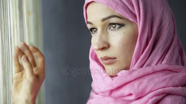 Bela mulher árabe muçulmano em hijab rosa olhando para fora da janela — Vídeo de Stock