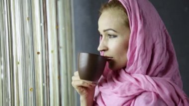 pembe hijab güzel Müslüman Arap kadını vurup pencere önünde içiyor.