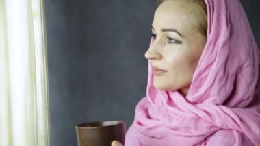 pembe hijab güzel Müslüman Arap kadını vurup pencere önünde içiyor.
