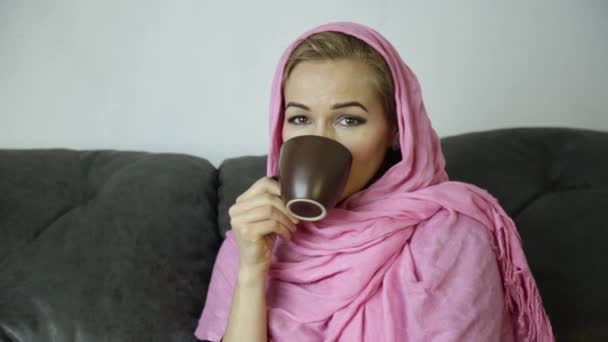 Beautiful arabian woman in pink hijab sitting on a sofa in a cafe and drinks cofee — Stock Video