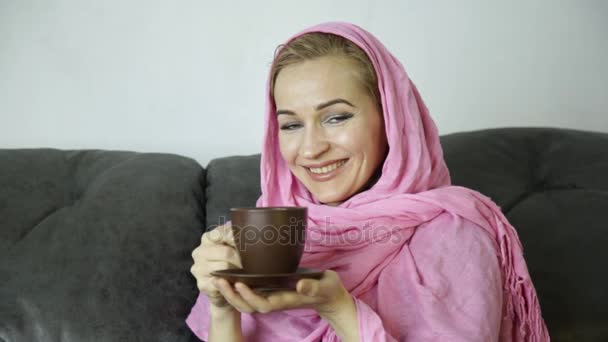 Красивая арабская женщина в розовом хиджабе сидит на диване в кафе и пьет кофе — стоковое видео