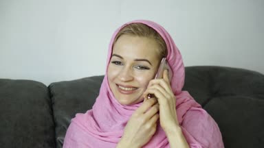 bir kafede bir kanepede oturan ve cep telefonuyla konuşurken pembe hijab güzel Arap kadını