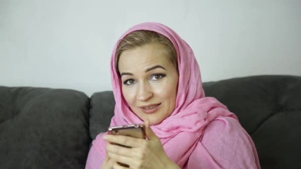 Mooie Arabische vrouw in roze hijab zittend op een bank in een café en stuurt een tekstbericht op mobiele telefoon — Stockvideo