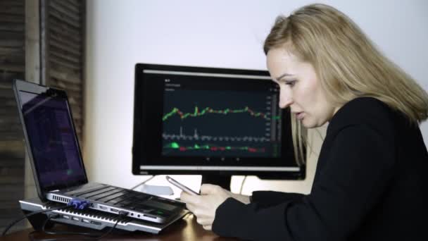 Vrouwelijke handelaar praten aan de telefoon en het kijken naar de grafiek van de uitwisseling van de valuta bij monitor van de computer. Werken op een crypto beurs — Stockvideo